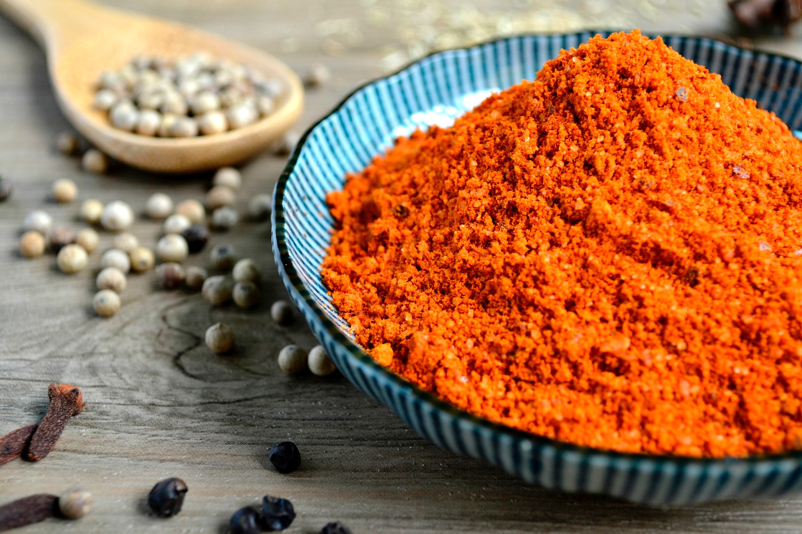 red spices on blue bowl with peppers scattered on table