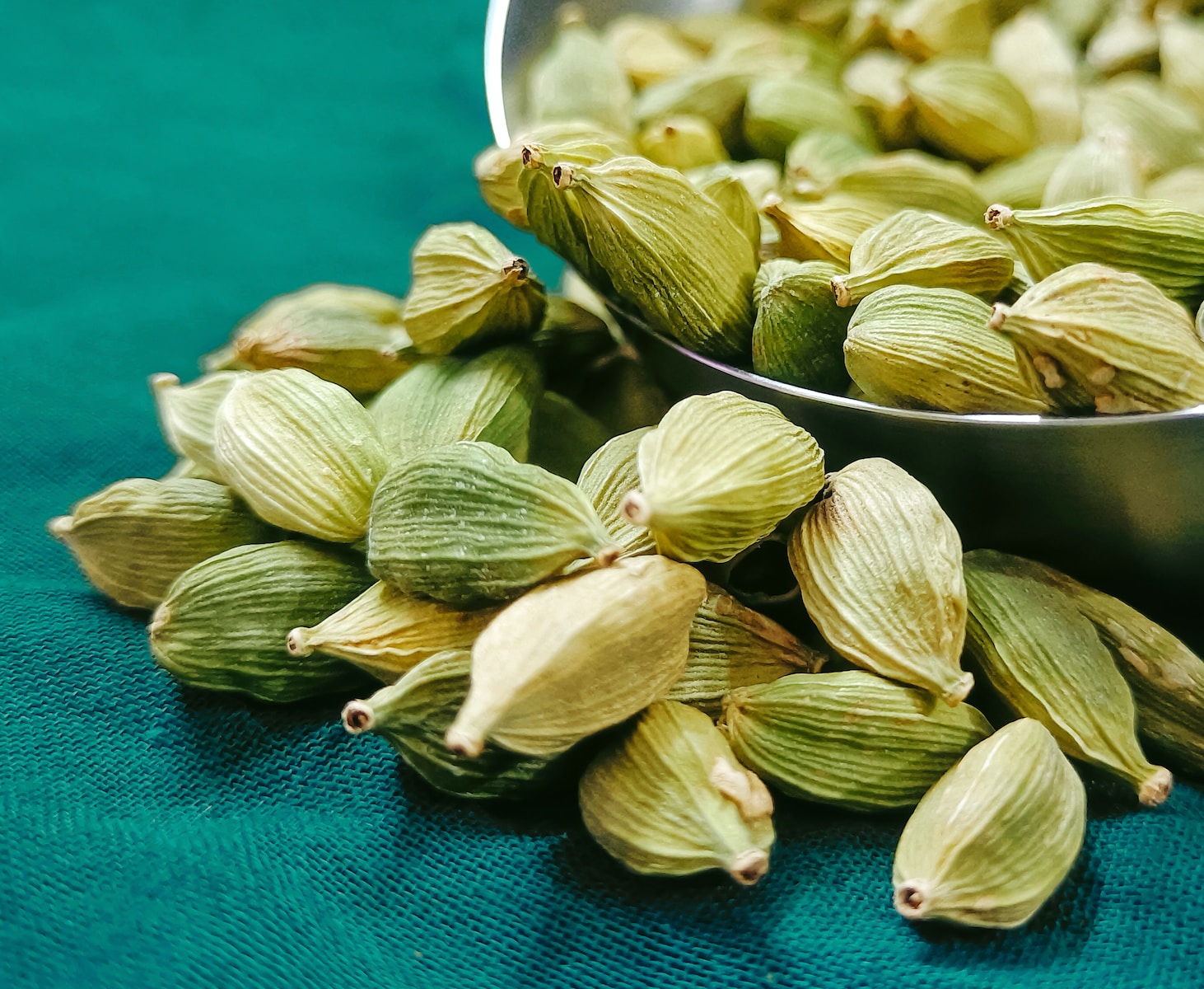 a metal bowl filled with green cardamom seeds