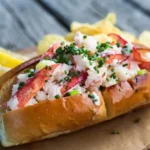 Fresh lobster roll recipe on a picnic table with lemon wedges and chips