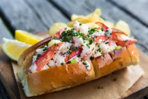 Fresh lobster roll recipe on a picnic table with lemon wedges and chips